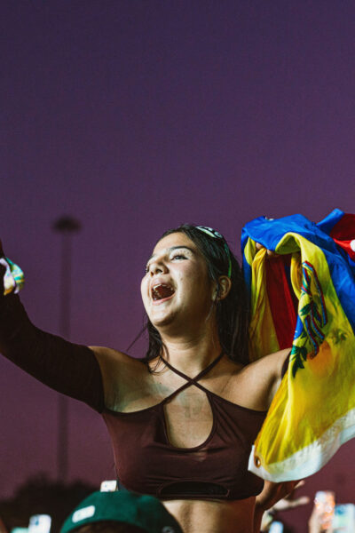 Vibra Urbana Miami 2022 Vibra Urbana Girl on shoulders holding phone at music concert holding flag
